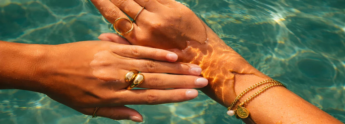 Hands in pool water wearing Priskel waterproof gold rings and bracelets