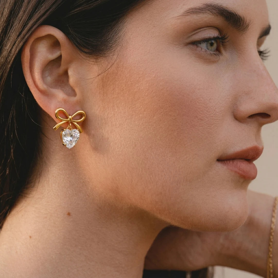 Celeste Bow Heart Earrings worn by a model in profile, waterproof gold bow earrings