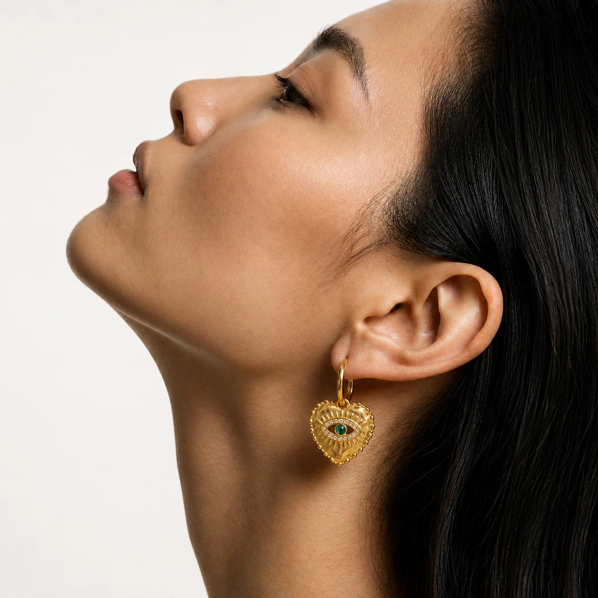 Nazar Heart Hoops worn by a model in profile, waterproof gold evil eye earrings