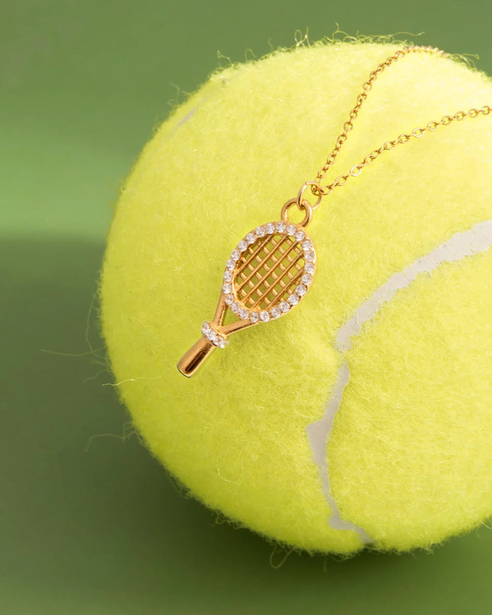 Pavé Tennis Racket Charm styled on a tennis ball against green – sweatproof, hypoallergenic charm