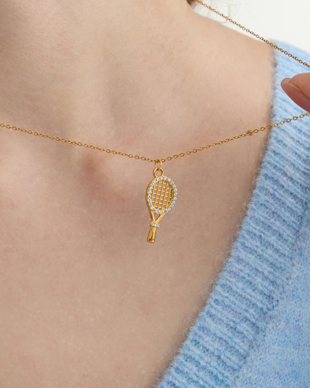 Pavé Tennis Racket Charm worn on a fine gold chain over a light blue knit, waterproof gold charm