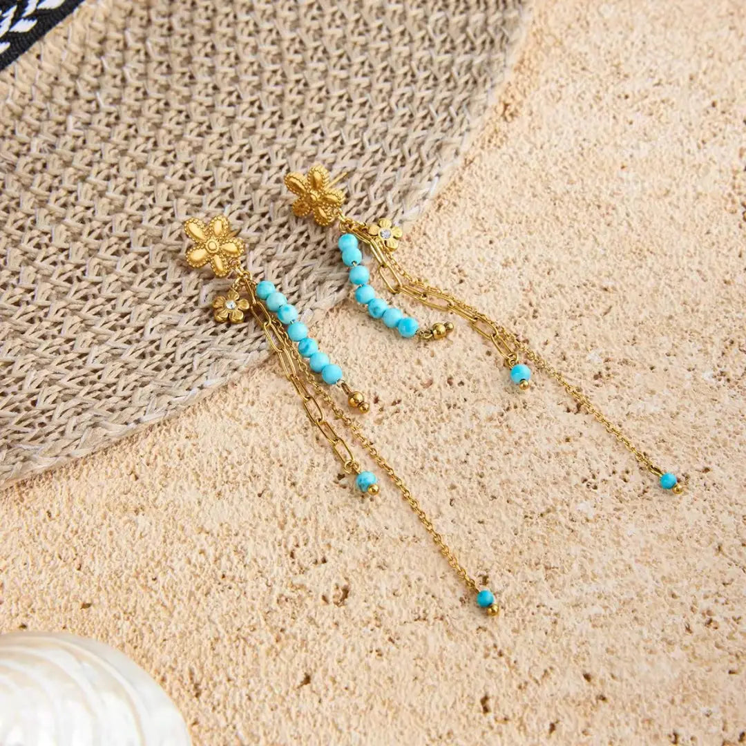 Turquoise Bloom Drop Earrings pair styled on a straw hat on sand, 18K gold PVD