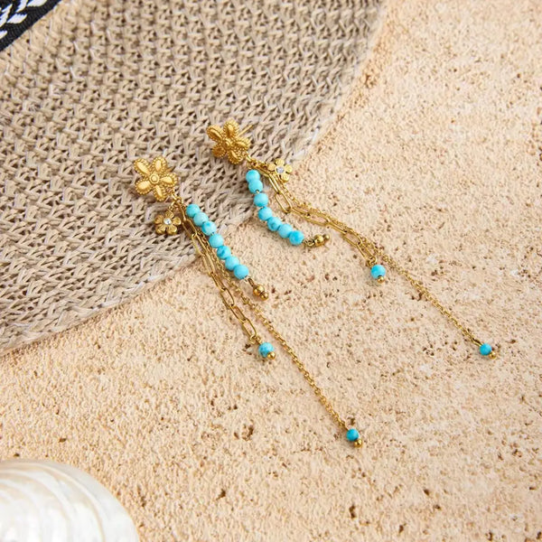 Turquoise Bloom Drop Earrings pair styled on a straw hat on sand, 18K gold PVD